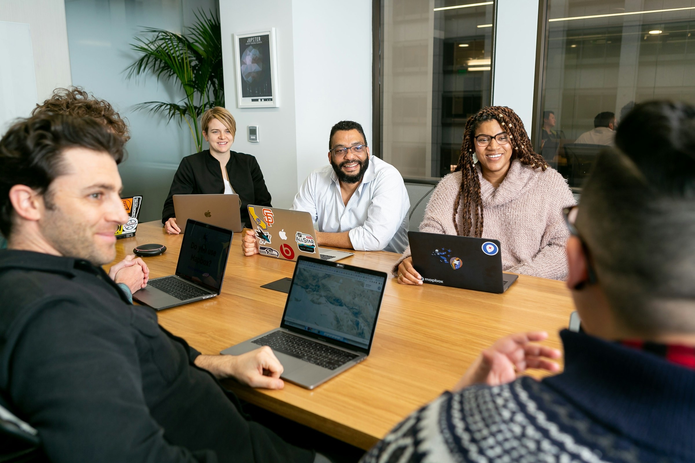 A diverse modern software team collaborating around laptops in a bright office.