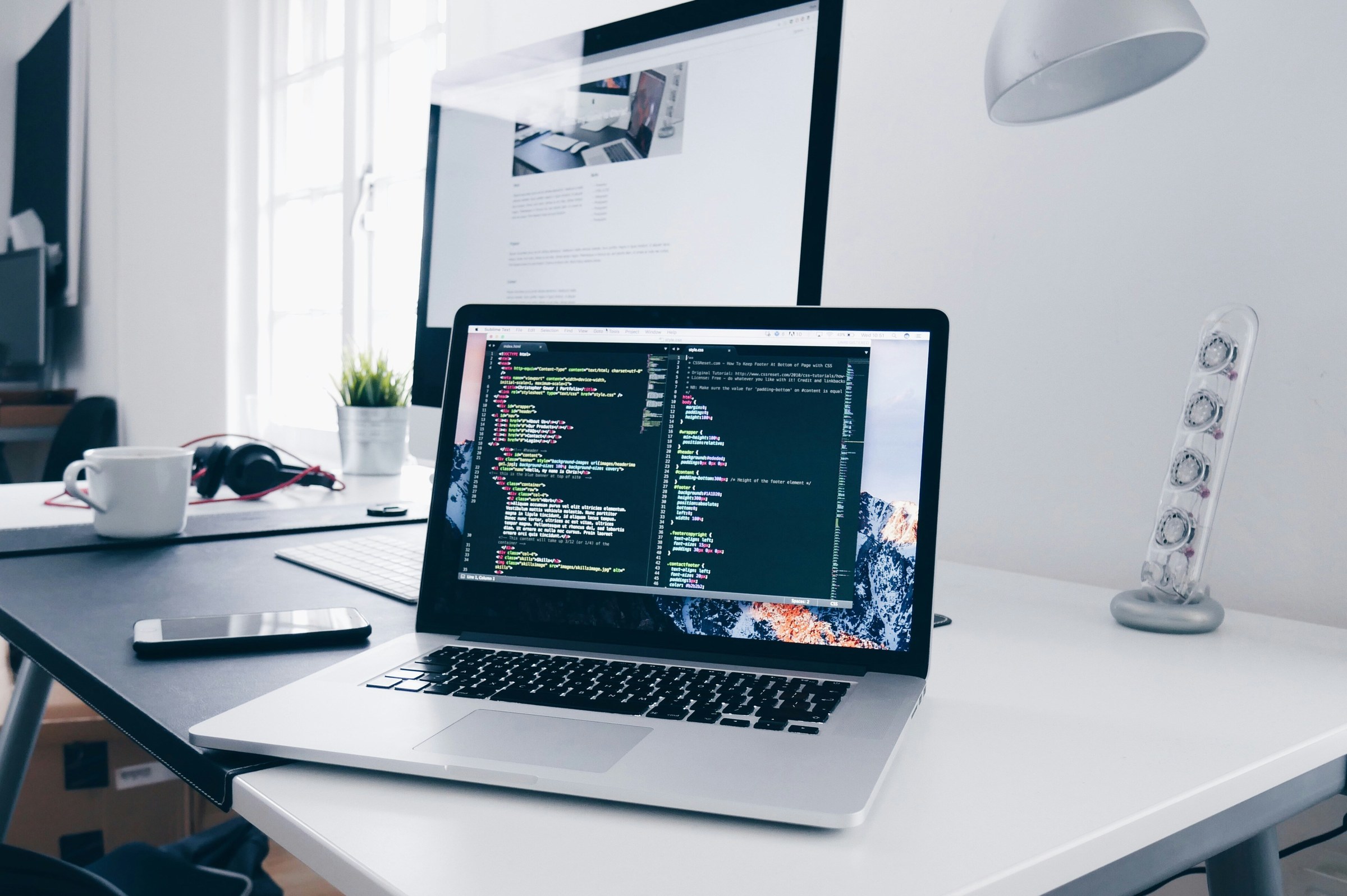 A laptop and external monitor on a modern desk, displaying code and a website in progress.